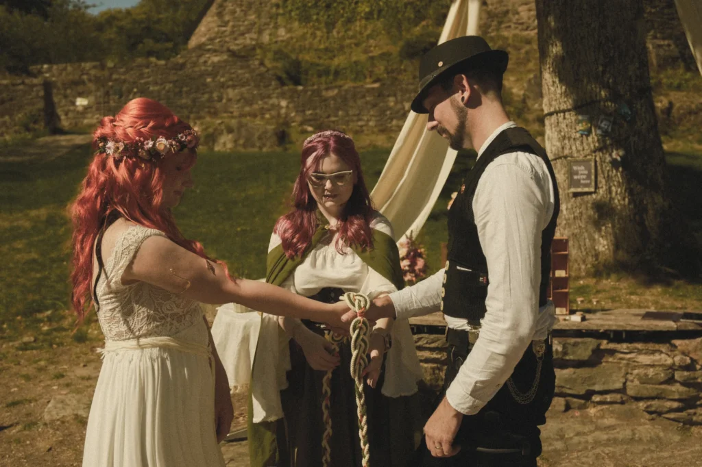 Traurednerin Bella bindet beim Handfasting auf der Burg Grimburg die Hände des Brautpaars mit einer geflochtenen Kordel.