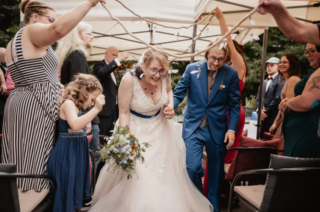 Das Hochzeitspaar läuft in der S'Kastanie in Heidelberg lachend unter der Girlande mit fliegenden Schlüsseln hindurch.